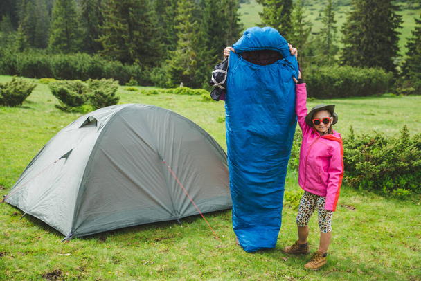 Little girl having fun with a sleeping bag near the tent in the mountains  - Foto, imagen