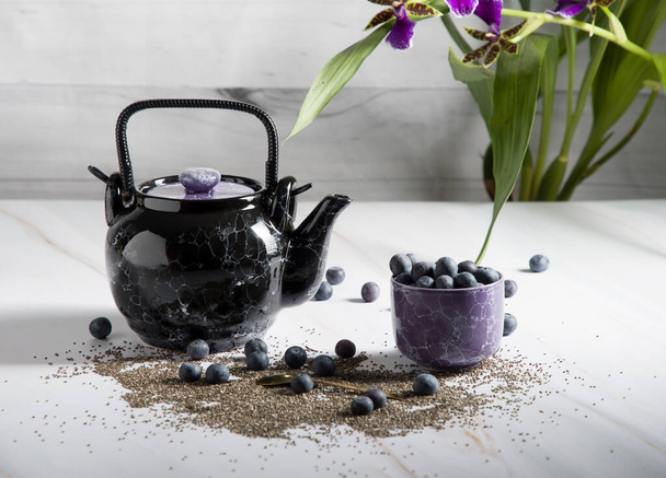 martwa natura z czarnym ceramicznym czajnikiem i deserem nasion chia, jogurtem i jagodami na jasnym tle z orchideą - Zdjęcie, obraz