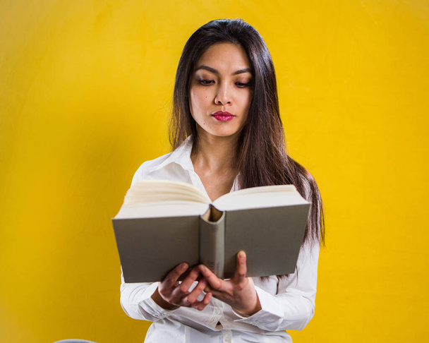 Young woman reading a book - studio shot against yellow background - Photo, Image