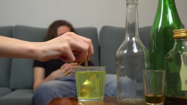Detailní záběr ženy trpící kocovinou, její přítelkyně nebo sestra míchající sklenici prášků proti bolesti vodou. Ženský alkoholismus. Na pozadí prázdných lahví, sklenic a sklenic. - Záběry, video