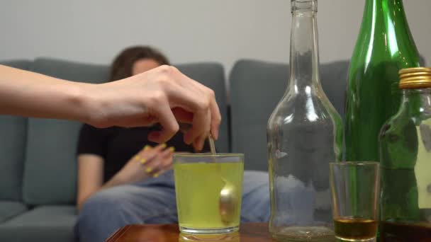 Detailní záběr ženy trpící kocovinou, její přítelkyně nebo sestra míchající sklenici prášků proti bolesti vodou. Ženský alkoholismus. Na pozadí prázdných lahví, sklenic a sklenic. - Záběry, video