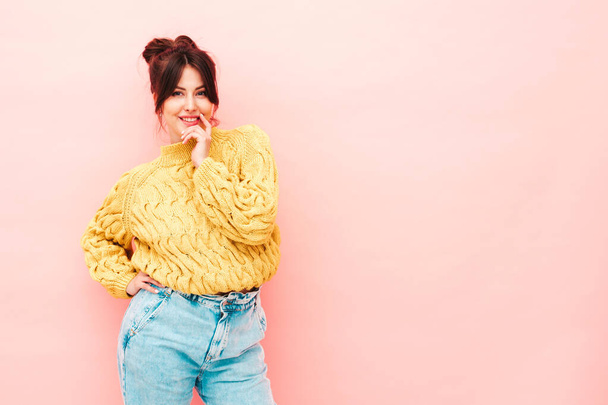 Young beautiful smiling female in trendy summer yellow hipster sweater and  jeans. Sexy carefree woman posing near pink wall in studio. Positive model having fun in sunglasses - 写真・画像