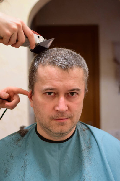 Um homem adulto é aparado com um cortador de cabelo e se senta de frente para a câmera. Talvez em casa em um confinamento - Foto, Imagem