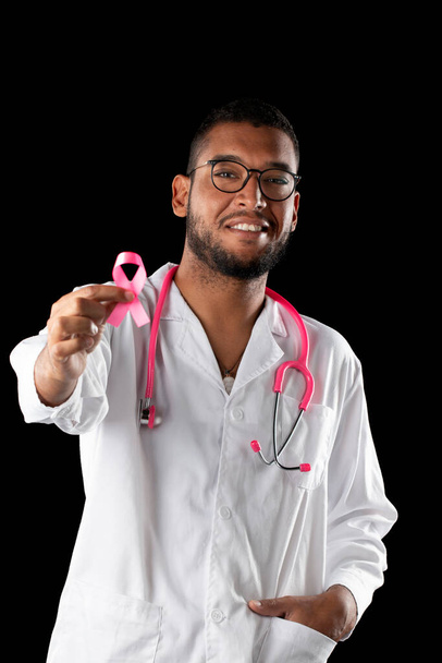 medico pelle scura con stetoscopio rosa e nastro rosa consapevolezza cancro al seno, su uno sfondo nero. - Foto, immagini