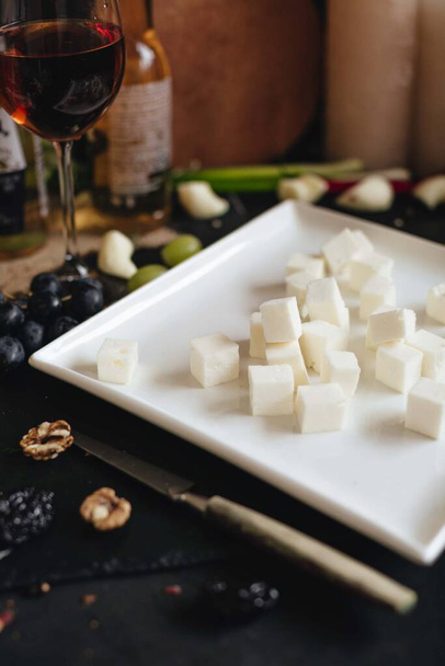 Montón de cubos de queso feta en un plato blanco en una mesa de cocina negro. - Foto, imagen