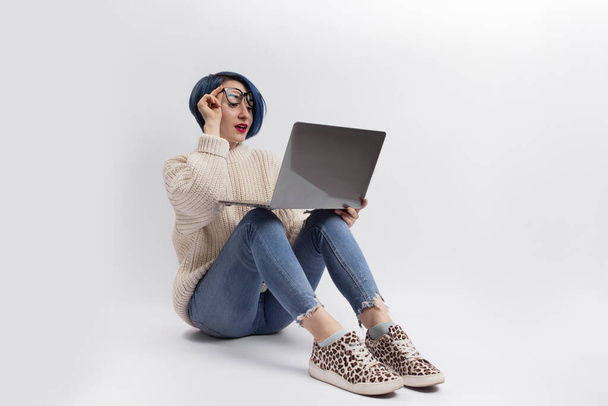 Eine Frau sitzt auf dem Boden und hält einen Laptop in der Hand. Isoliert - Foto, Bild