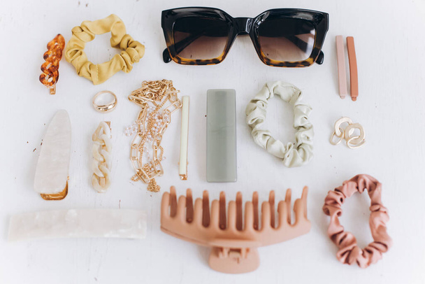 Modern summer accessories layout. Golden jewellery, sunglasses, hair clips and hairbands, barrettes on white table top view. Feminine essentials. Boho colorful accessories - Photo, Image