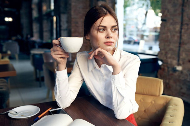 piękna kobieta z kubkiem w ręku siedzi przy stole w kawiarni i zarezerwować restaurację - Zdjęcie, obraz