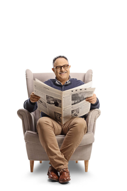 Cheerful mature man reading a newspaper and smiling seated in an armchair isolated on white background - Foto, immagini