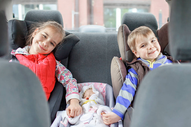 Sisarus istuu turvaistuimilla ja pitelee nukkea myös auton istuimella käsin, lasten kuljetusturvallisuus - Valokuva, kuva