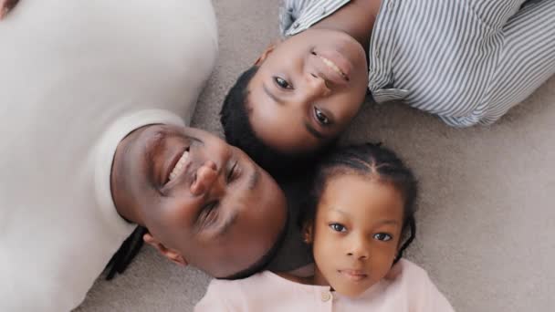 Портрет афроамериканських батьків з маленькою донькою лежить на підлозі, дивлячись на усміхненого дорослого батька-афроамериканця, який вказує на камеру пальцем, вгорі, на три покоління. - Кадри, відео