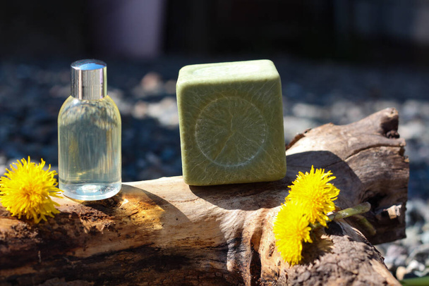 Чистая косметическая бутылка и натуральное зеленое мыло, стоящее на дереве в солнечный день - Фото, изображение