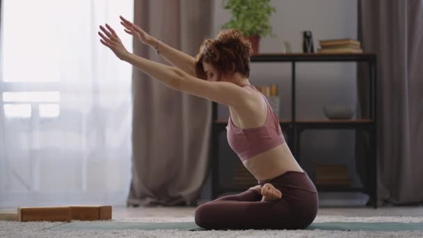 утренние упражнения и йога тренировки, женщина сидит в позе лотоса на полу в квартире, делая упражнения для растяжения - Кадры, видео
