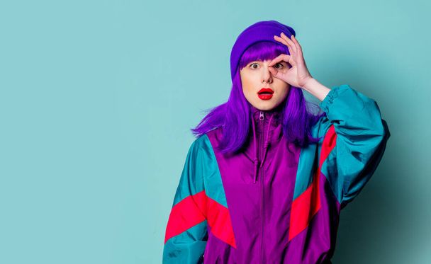 Surprised white girl with purple hair and 80s tracksuit on blue background - Фото, изображение