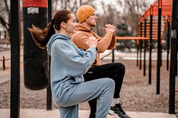 Młoda para w sportowym stroju ćwiczy na świeżym powietrzu. Młody mężczyzna i kobieta rozciągający mięśnie przed bieganiem po boisku sportowym. Pozostawanie w formie i zdrowa koncepcja. - Zdjęcie, obraz