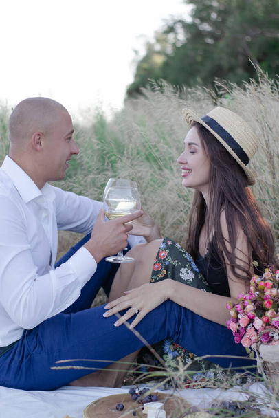 Mann und Frau bei einem romantischen Date auf einem Picknick und trinken Wein. brünett und glatzköpfig im Feld. Glückliches Paar. - Foto, Bild