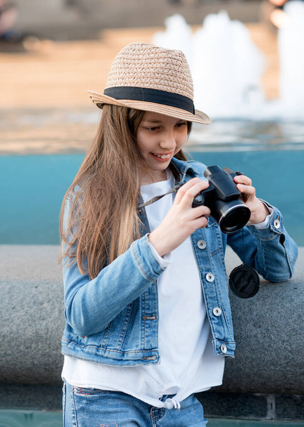 Dívka v džínovém kabátě, slaměný klobouk a džíny s kamerou procházka po centru města a fotografování - Fotografie, Obrázek