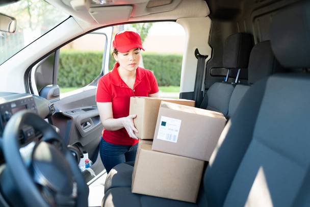 Caucasian female courier searching for a package inside a delivery van. Delivery woman working and choosing a parcel to deliver at a shipping address - Photo, Image