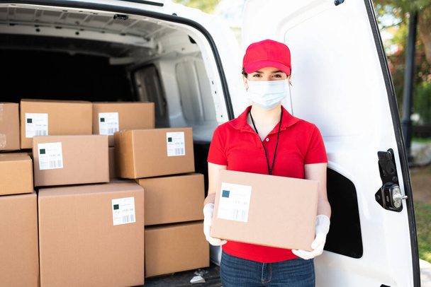 Retrato de un trabajador caucásico con una máscara facial y guantes mientras hace un servicio de entrega y lleva un paquete durante la pandemia de coronavirus - Foto, imagen