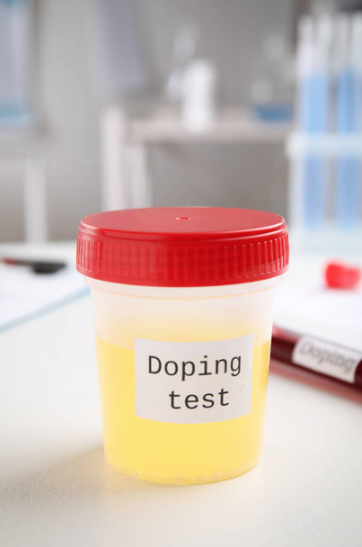 Jar with urine sample on white table indoors. Doping control - 写真・画像