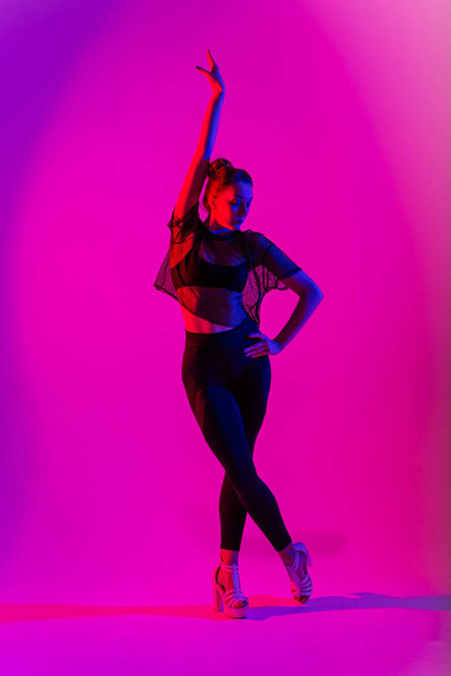 Schöne Tänzerin, die schwarze High Heels trägt, während sie Poledance-Tricks aufführt, Neon - Foto, Bild