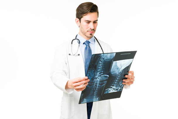 Especialista médico examinando la radiografía de un paciente con un hueso roto. Médico ortopédico con una bata blanca mirando un escáner sobre un fondo blanco - Foto, Imagen