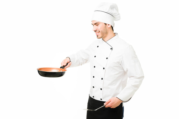 Junger Koch kocht ein köstliches Abendessen in einem Restaurant. Attraktive lateinamerikanische Köchin braten ein neues Gericht mit Pfanne und Spachtel vor weißem Hintergrund - Foto, Bild