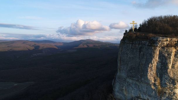 Croix d'or sur un sommet de montagne avec une pente raide, concept de religion. Fusillade. Vue aérienne d'une falaise et d'une belle vallée vallonnée sur le fond. - Photo, image