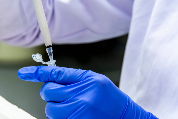 Wissenschaftler pipettiert die Probe in die Röhre, während er Schutzhandschuhe für die Impfstoffforschung trägt - Foto, Bild