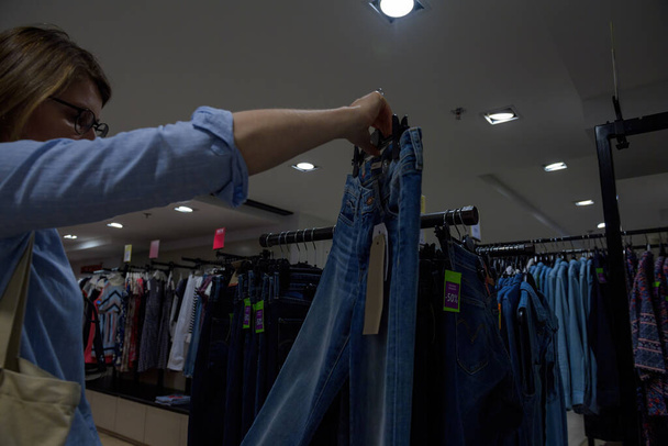 Woman shopping inside store for new pair of jeans - measuring in the air the luxury bio blue denim garment - Photo, Image