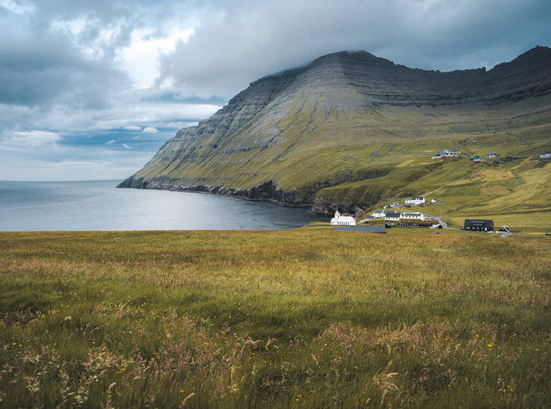 View onto the church of Vidareidi also named Vidareidi Kirkja with moody cloudy sky, fog and mountains. Faroe Islands, Denmark, Europe. - Foto, afbeelding