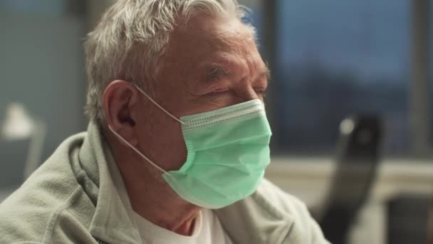 Een close-up portret van een oudere man met een medisch masker op zijn gezicht - Video