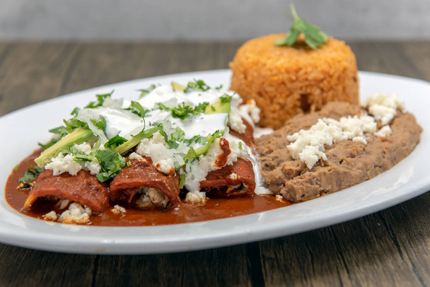 Kırmızı soslu tavuk enchilada. Lezzetli bir Meksika yemeği için kızarmış fasulye ve pilav ile servis edilir.. - Fotoğraf, Görsel
