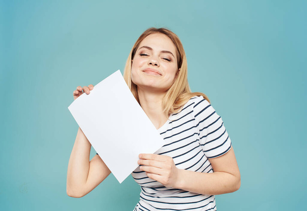 Tunteellinen blondi nainen, jolla on valkoinen paperiarkki käsissään sinisellä taustalla - Valokuva, kuva