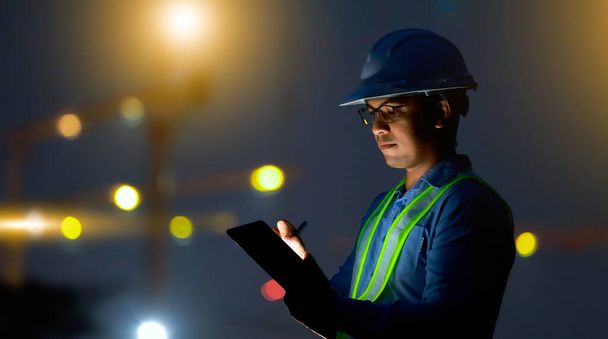 Ingeniero utilice tableta digital en el sitio de construcción por la noche - Foto, imagen