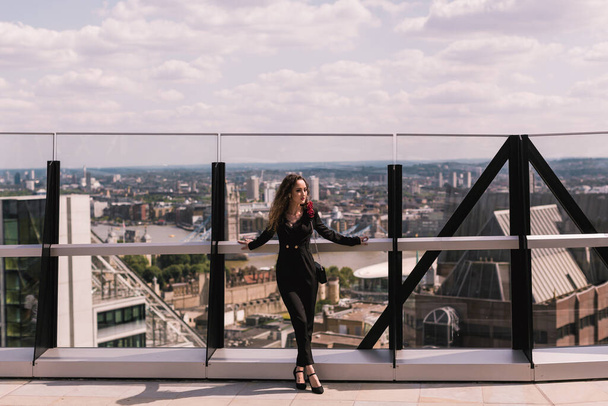 Stylish business lady in a classic black suit. In full growth. Beauty. Background buildings, city landscape. Sky terrace. Skyscrapers. - Valokuva, kuva