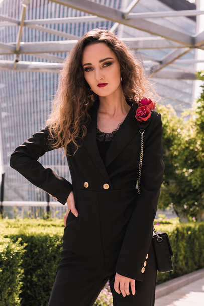 Portrait of stylish business lady in a classic black suit. Beauty. Background glass buildings. Sky terrace. Skyscrapers. - Fotó, kép