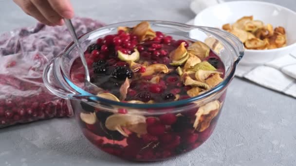 Vaření domácí zdravé nápoje nebo kompot ze sušených jablek a zmrazených bobulí na lehkém pozadí - Záběry, video