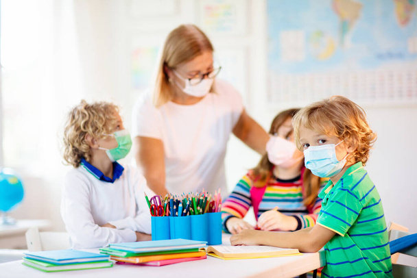 Δάσκαλος στην τάξη, σχολιαρόπαιδο με μάσκα προσώπου κατά τη διάρκεια του ιού του κόρωνα και ξέσπασμα γρίπης. Αγόρι και κορίτσι πίσω στο σχολείο μετά την καραντίνα και τον αποκλεισμό του Covid-19. Ομάδα παιδιών με μάσκες για την πρόληψη του ιού της στέψης. - Φωτογραφία, εικόνα