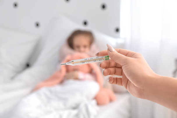 Γυναίκα μέτρηση της θερμοκρασίας της μικρής της κόρης άρρωστος με γρίπη στην κρεβατοκάμαρα - Φωτογραφία, εικόνα