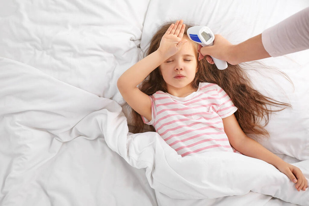 Kobieta mierzy temperaturę swojej córeczki chorej na grypę w łóżku - Zdjęcie, obraz