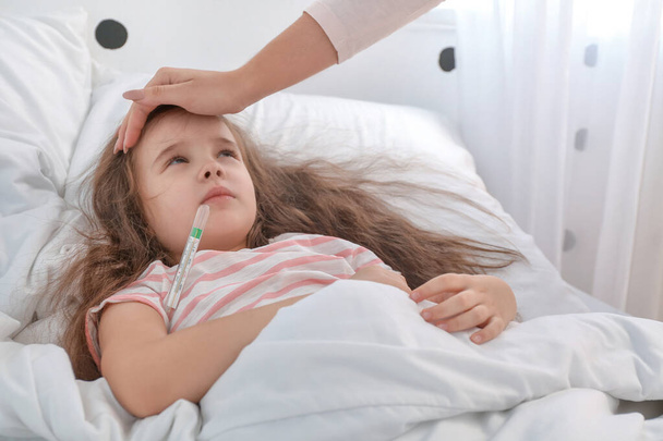 Femme mesurant la température de sa petite fille malade de la grippe dans la chambre - Photo, image