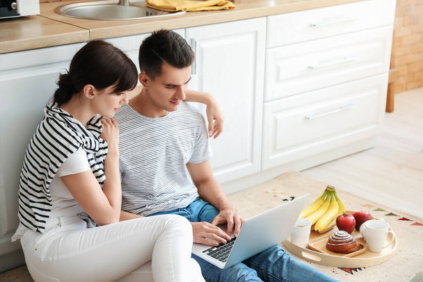 Ευτυχισμένο νεαρό ζευγάρι με φορητό υπολογιστή στην κουζίνα - Φωτογραφία, εικόνα