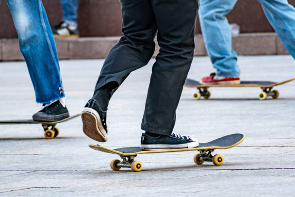 Молодые люди или подростки катаются на скейтборде в городе, вид снизу на спортивную обувь и скейтборды  - Фото, изображение