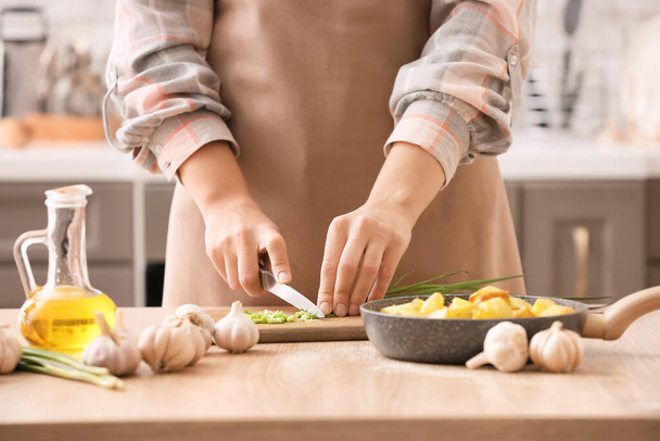 Mujer cortando cebolla verde en la mesa en la cocina - Foto, imagen