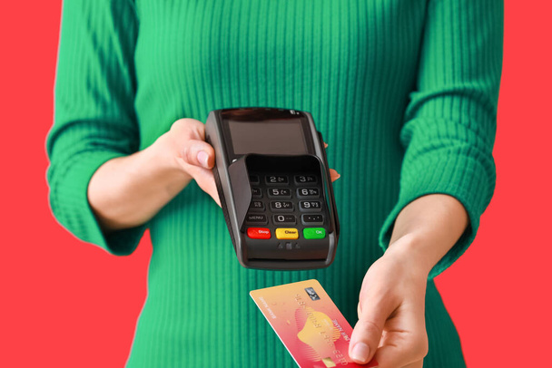 Young woman with payment terminal and credit card on color background, closeup - Φωτογραφία, εικόνα