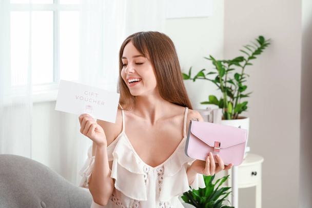 Beautiful young woman with gift voucher and bag at home - Foto, afbeelding