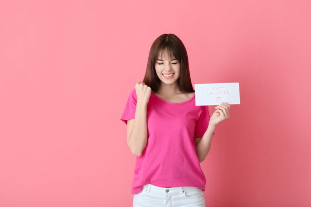 Happy young woman with gift voucher on color background - Photo, Image
