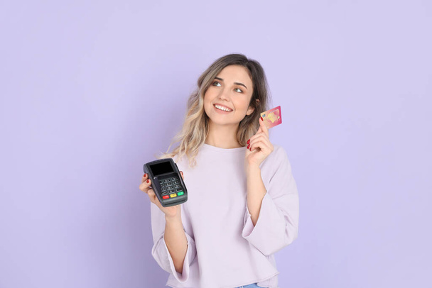 Young woman with payment terminal and credit card on color background - Photo, Image