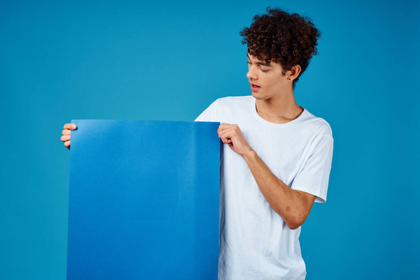Beyaz tişörtlü bir adam elinde mavi arka plan reklamları yapan bir poster tutuyor. - Fotoğraf, Görsel